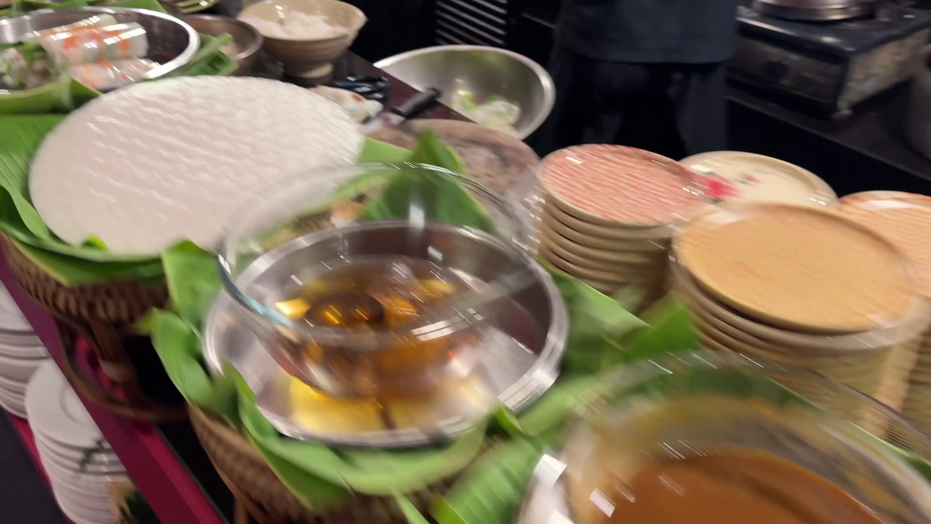 Busy kitchen prep counter at Nhà Hàng Ngon with banana leaves, stacked plates, and cooking condiments