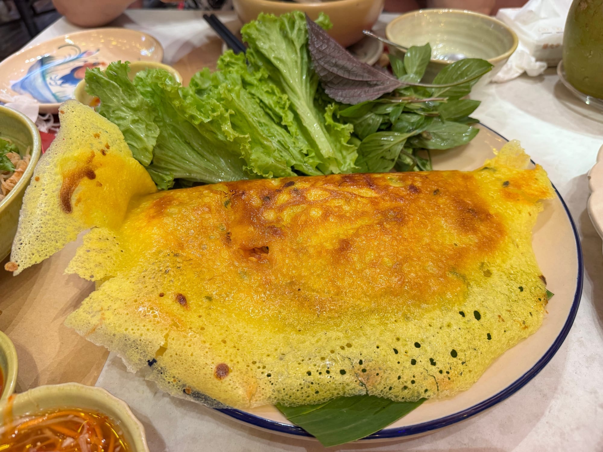 Golden Vietnamese banh hoai crepe served with fresh herbs and lettuce