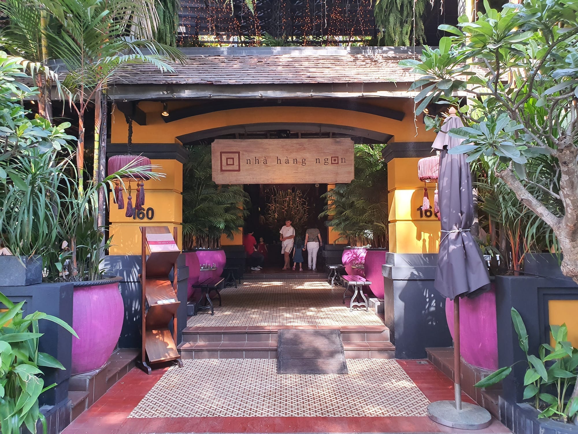 Colourful orange and magenta entrance to Nhà Hàng Ngon surrounded by tropical plants