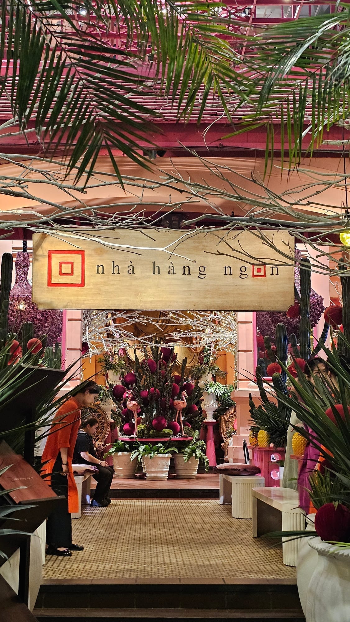 Nhà Hàng Ngon entrance with hanging palm fronds and burgundy floral arrangements above the wooden storefront